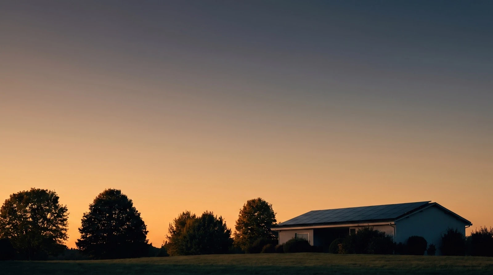 Silhouetted trees and a barn against an orange sunset