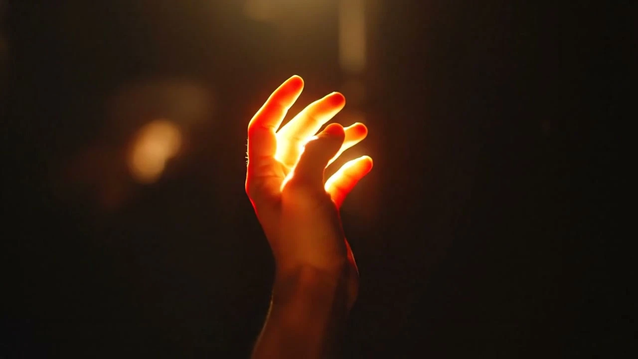 Hand reaching toward a glowing orange light in the dark